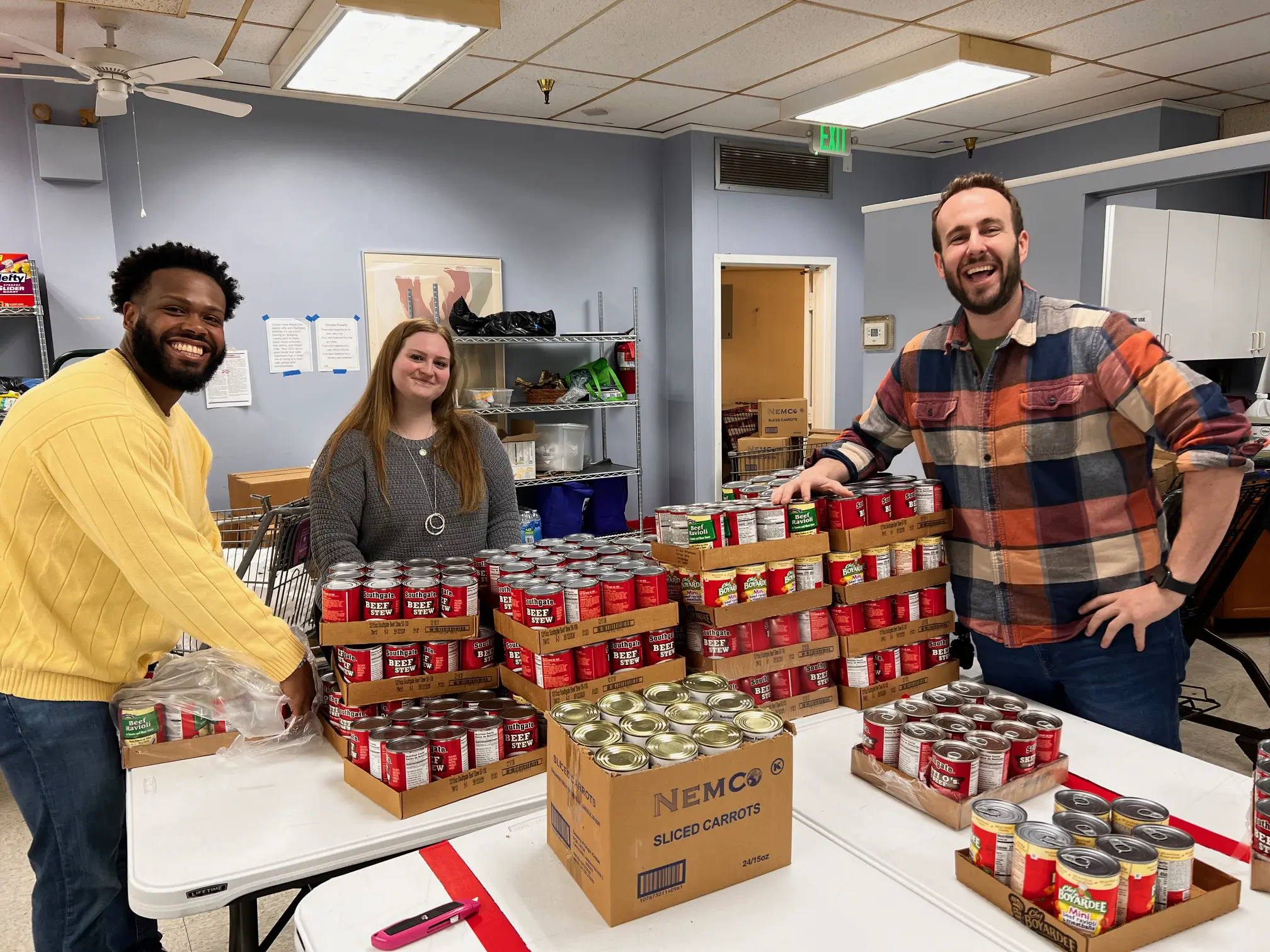 Three people smiling while opening cases of cans.