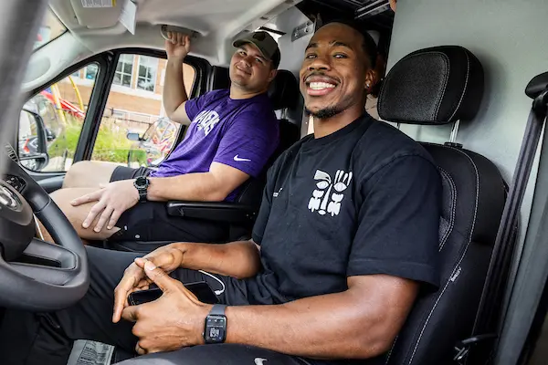 Two Ravens players in the driver and passenger seat of the Weekend Backpacks van