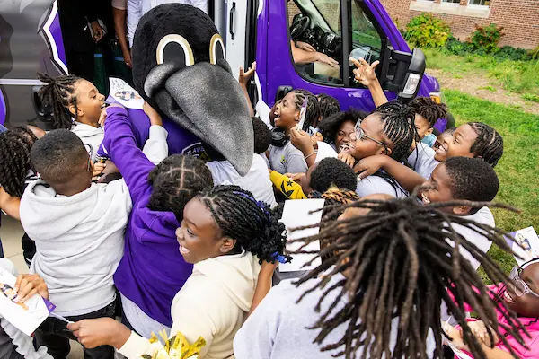 Ravens mascot, Poe, greeting students in front of the Weekend Backpacks van