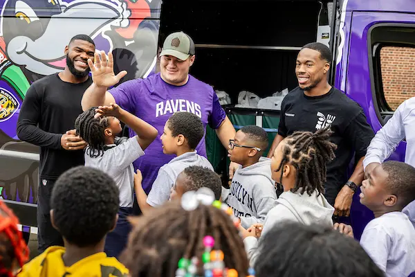 Ravens players greeting students in front of the Weekend Backpacks van