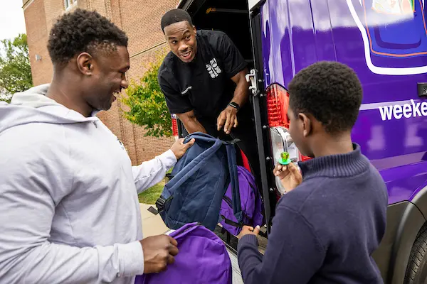 Ravens players handing backpacks out of the Weekend Backpacks van to a student