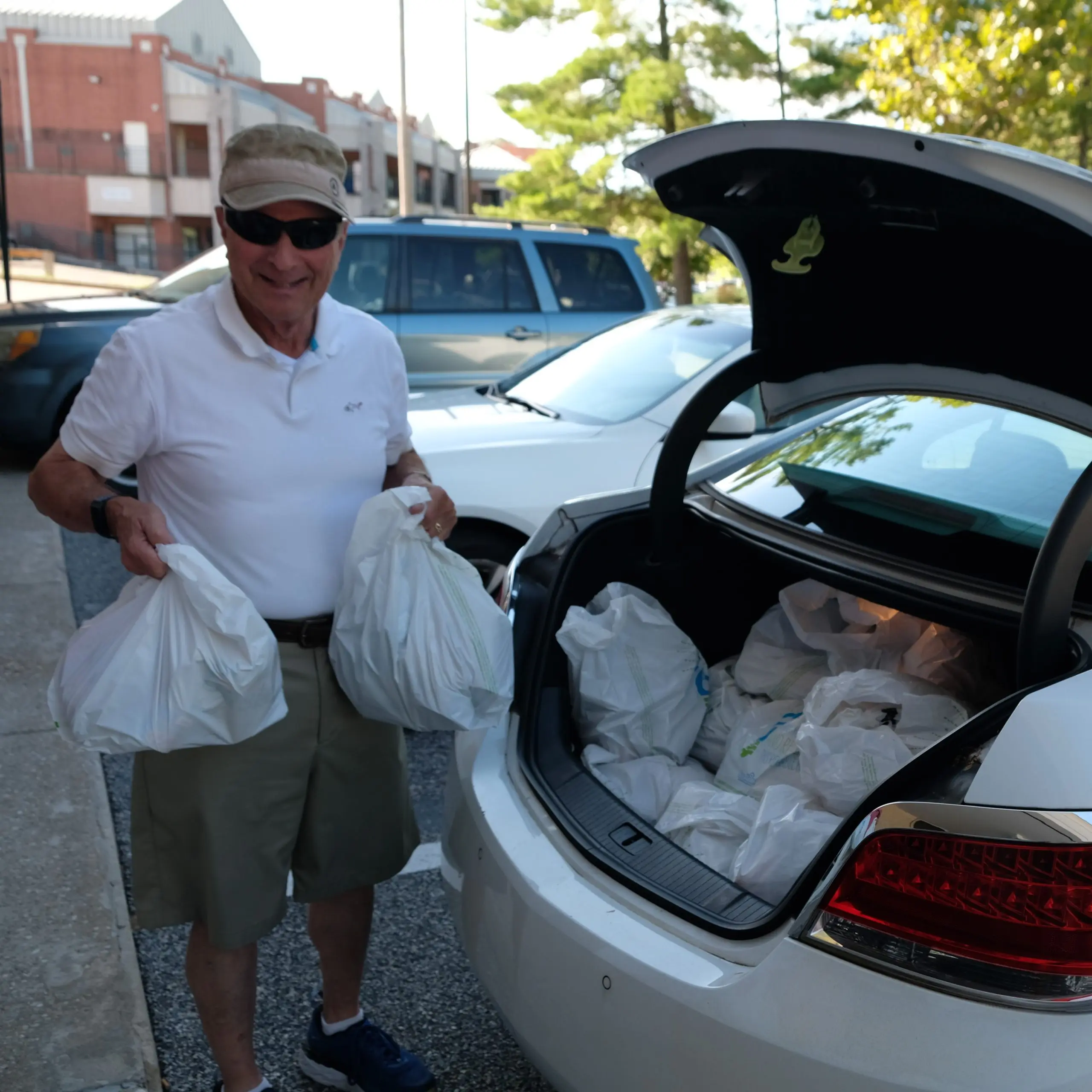 A man standing outside loading bags of food into the trunk of a car.