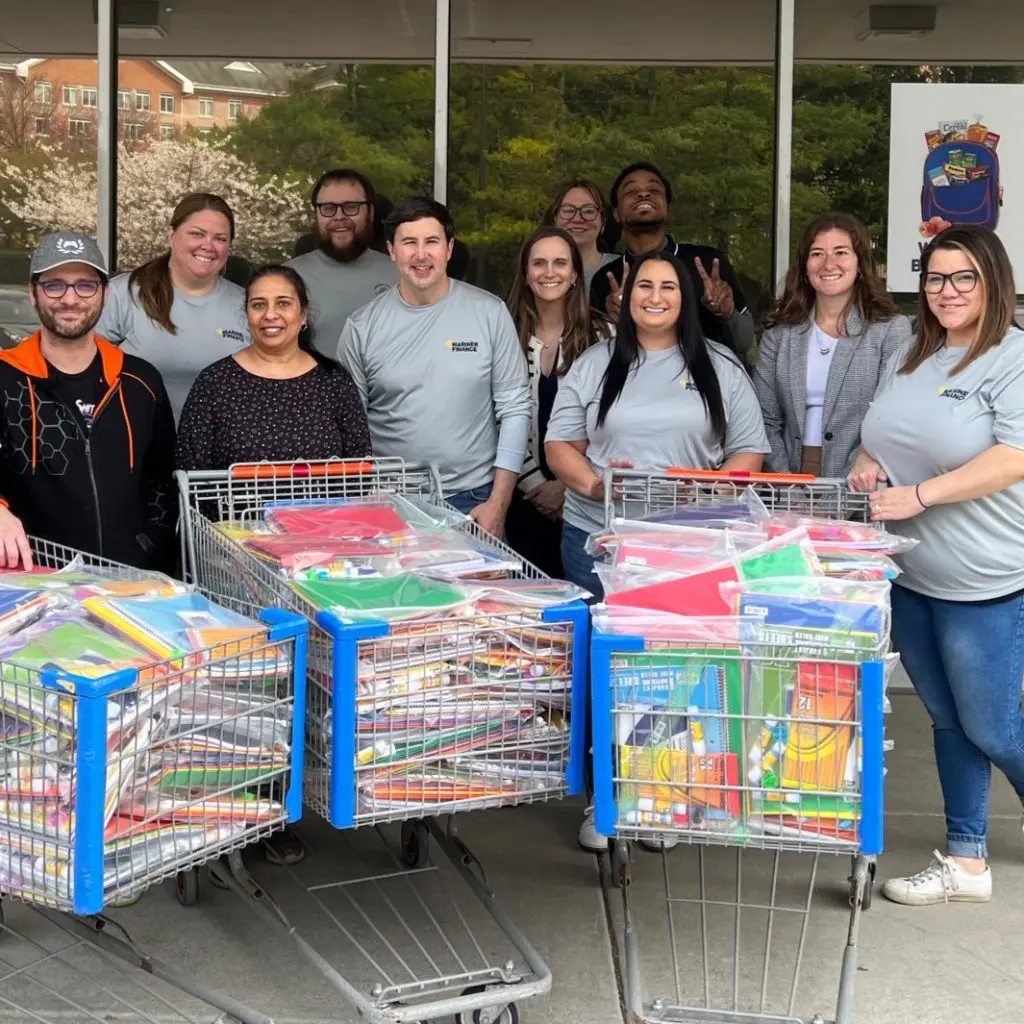 A group of people outside of Weekend Backpack's facility with shopping carts of packed bags of school supplies.