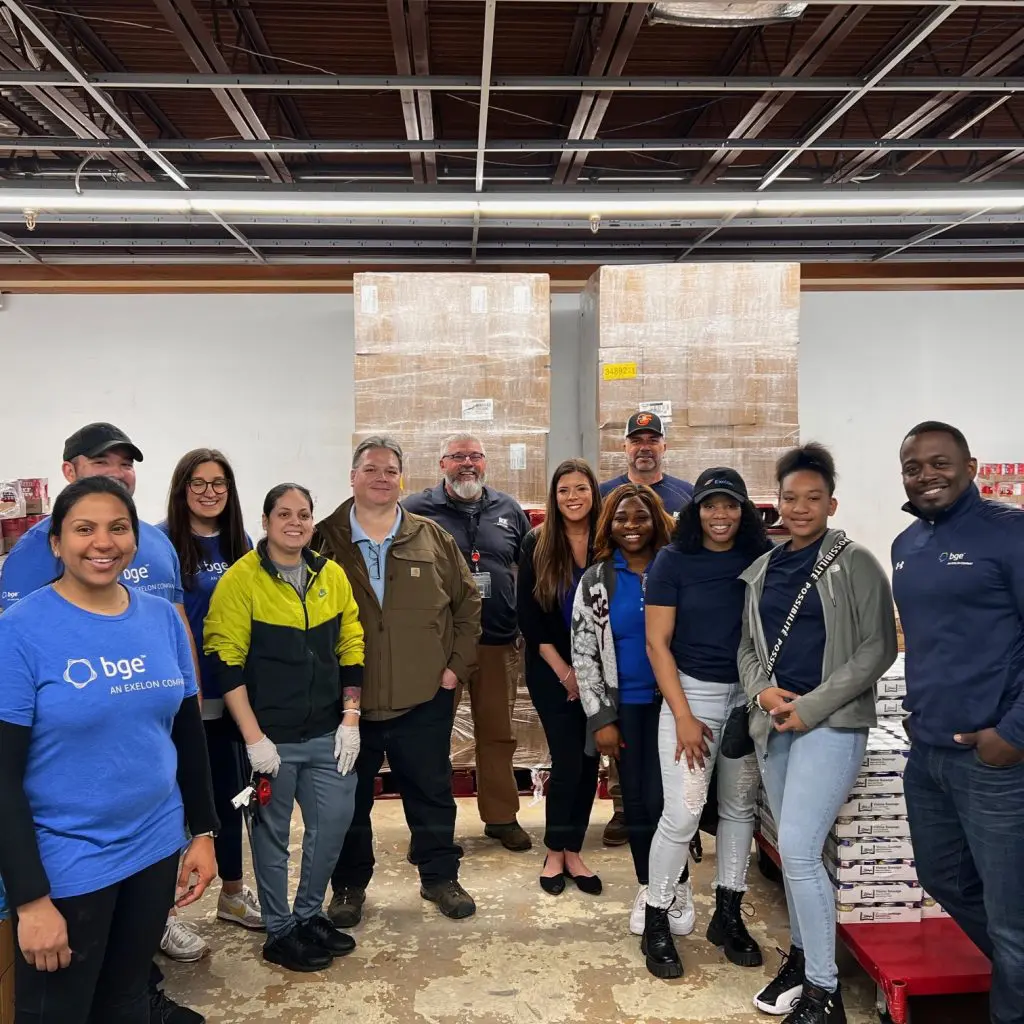 A group of people posed in a stock room with pallets of food.