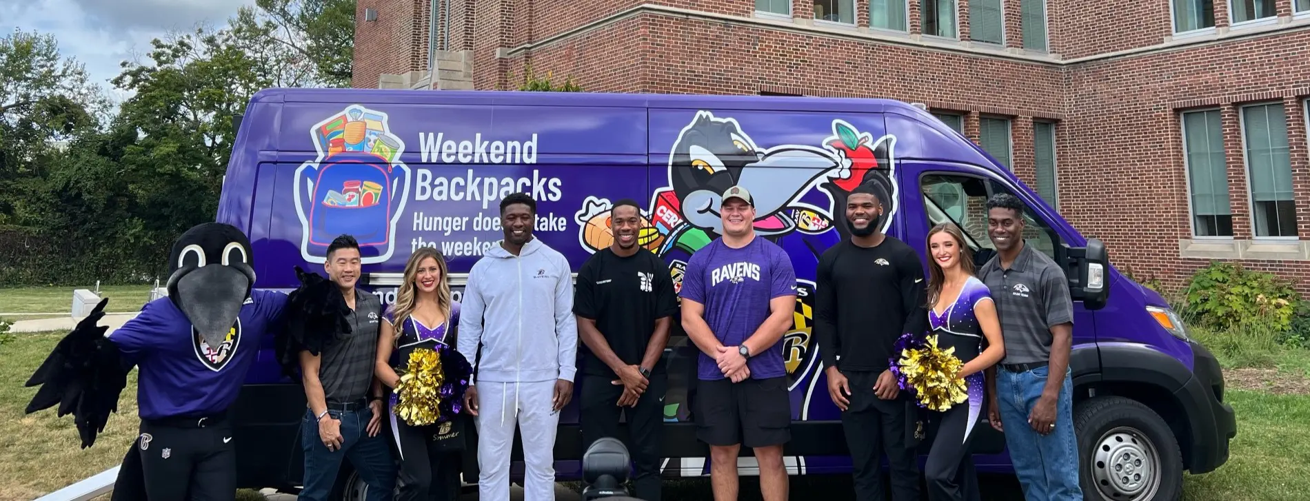 Ravens players, cheerleaders, and mascot in front of the Weekend Backpacks' van