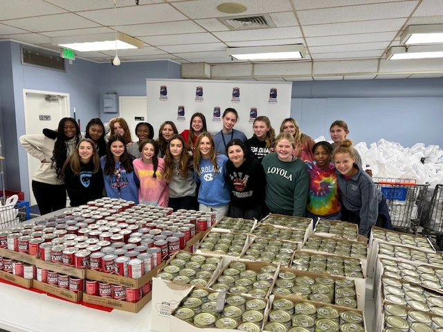 A group of students posed behind a table with cases of food on it.