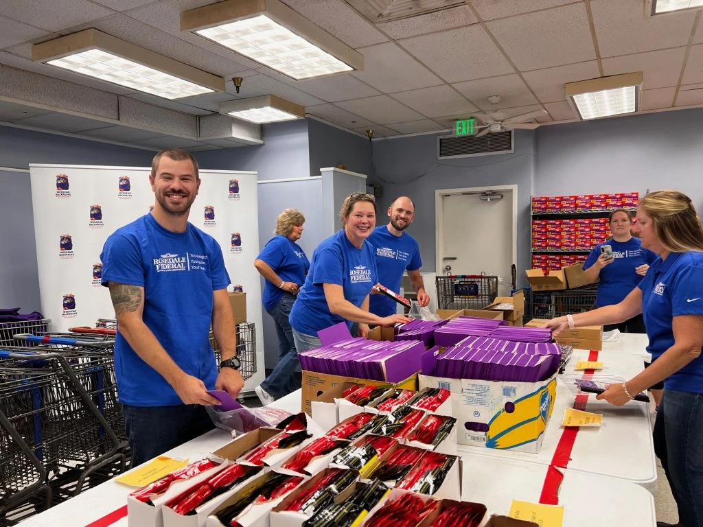 People around a table packing bags of school supplies.