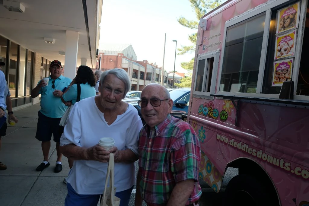 Two people standing in front of the Deddles Donuts truck smiling.