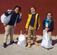 Three young boys standing outside smiling and holding bags of food.