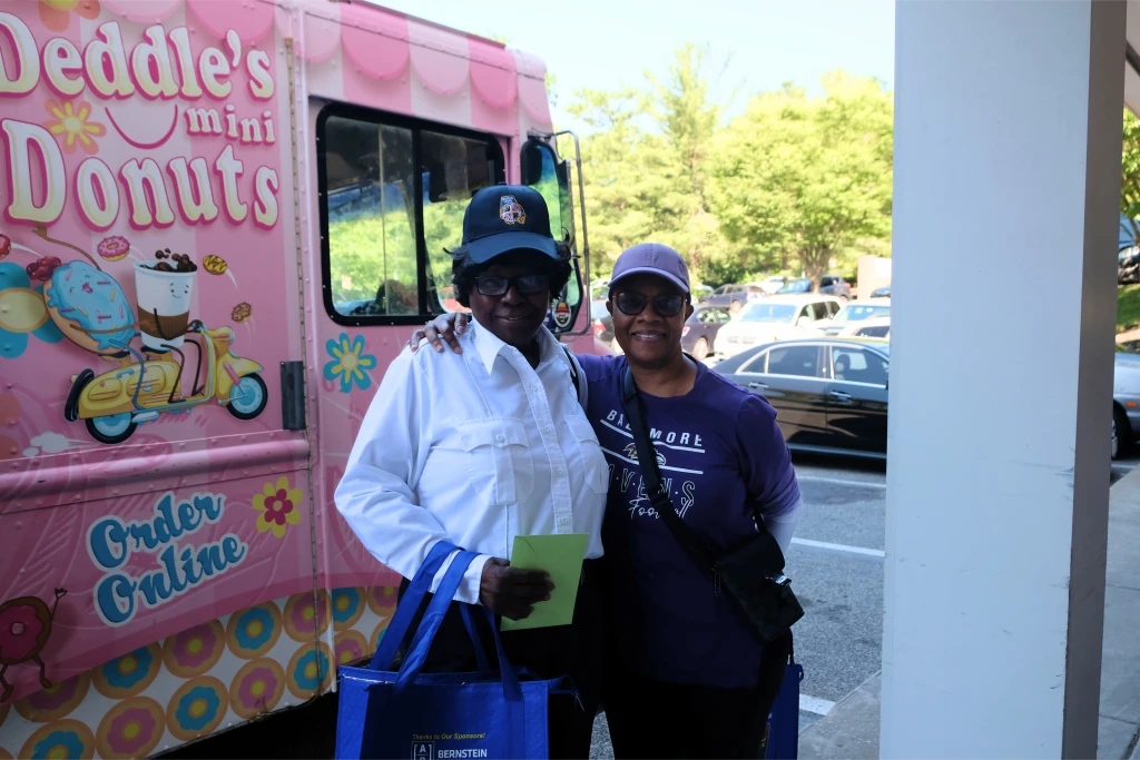 Two women smiling in front of a truck reading "Deddle's mini donuts."