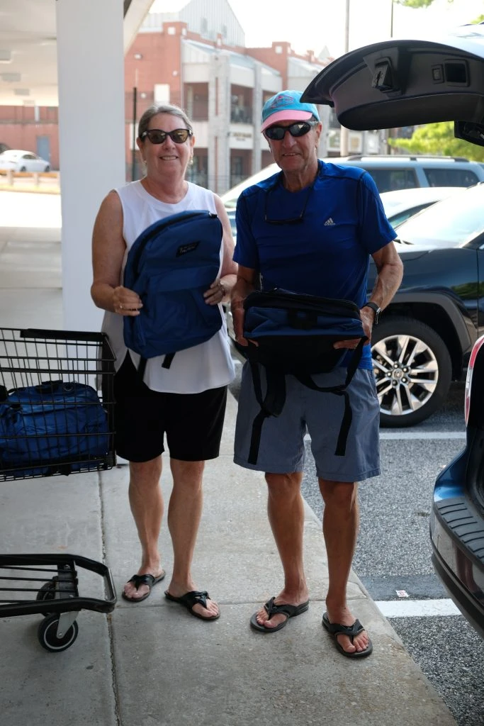 Two people holding backpacks as they load them into the trunk of their car.