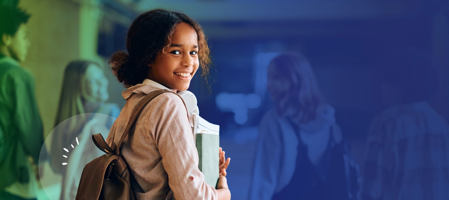 A young girl with a backpack on holding books in a school hallway.