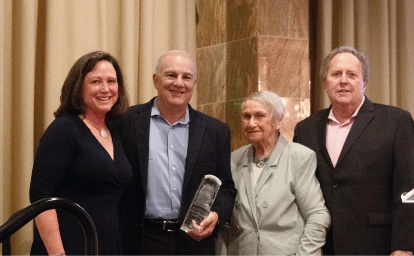 Four people posed smiling with one of them holding an award.