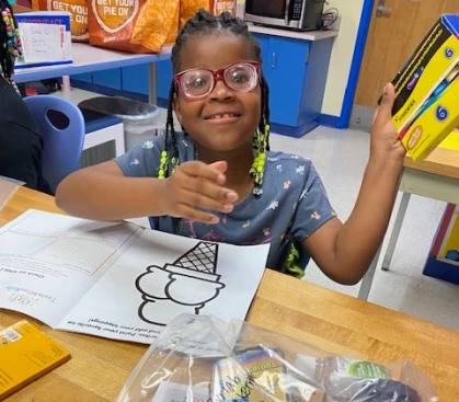 A young student sitting at a table with a coloring book.