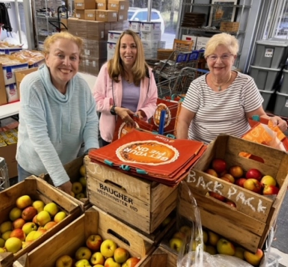 Three women standing behind crates of apples.