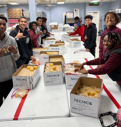 A group of boys smiling around a table with boxes of fruit cups.