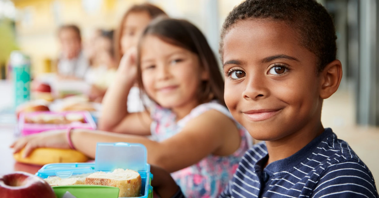 Young students sitting at a table with their lunches.