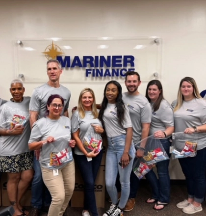 A group of people holding plastic bags of snacks in front of a "Mariner Finance" sign.