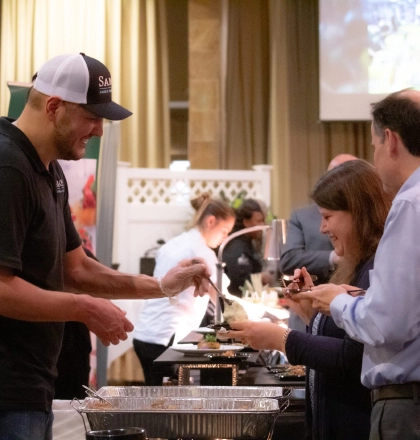 A chef serving two patrons across a table.