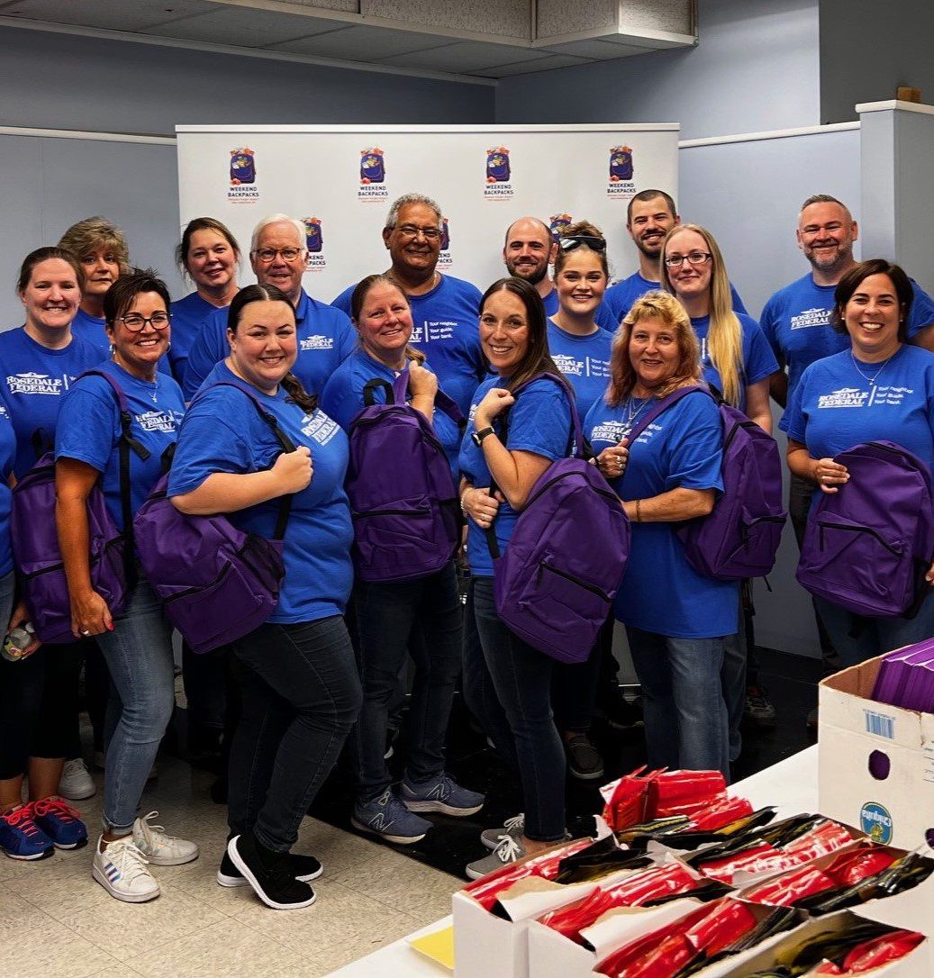 A group of people posing holding backpacks.