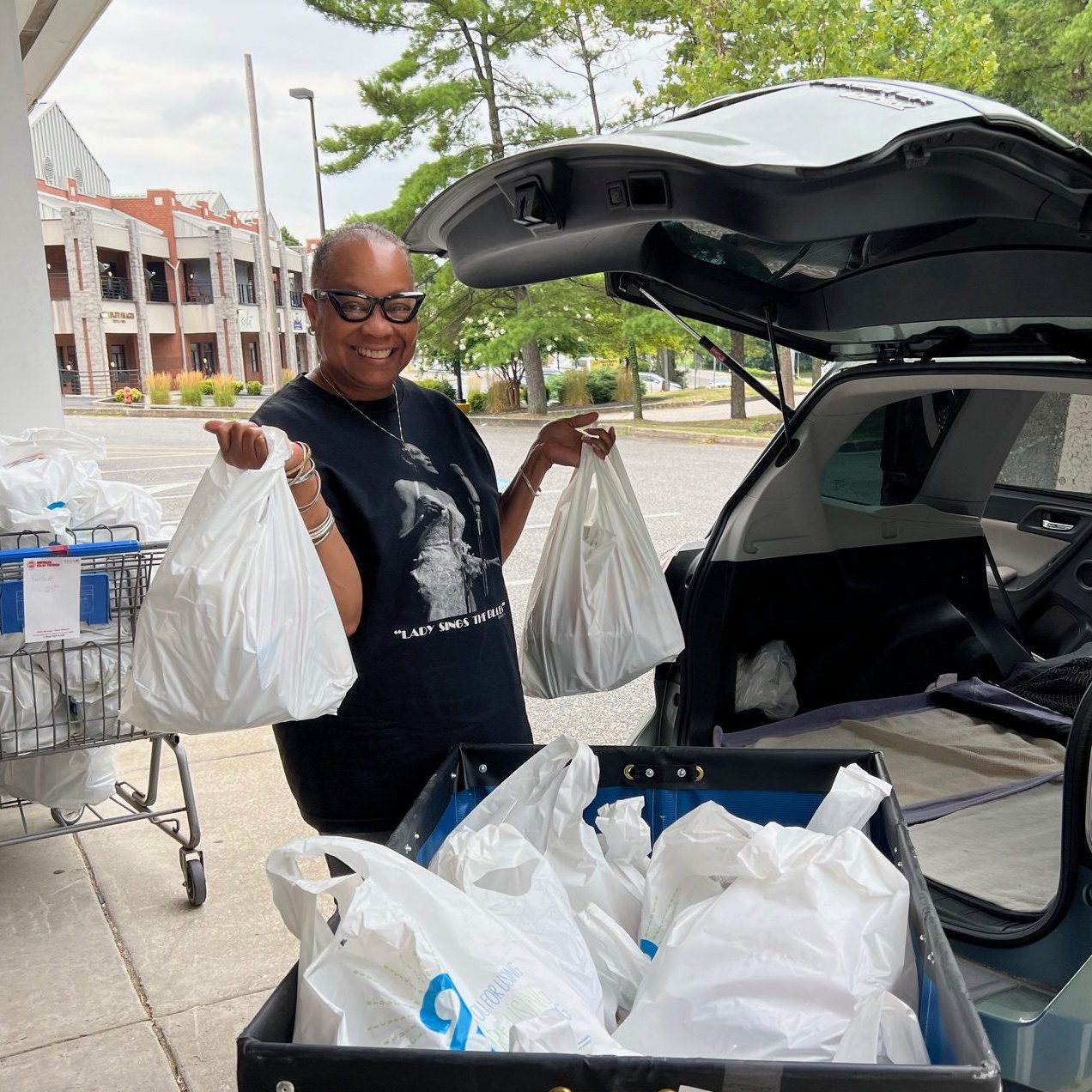 A woman loading bags of food into her trunk.