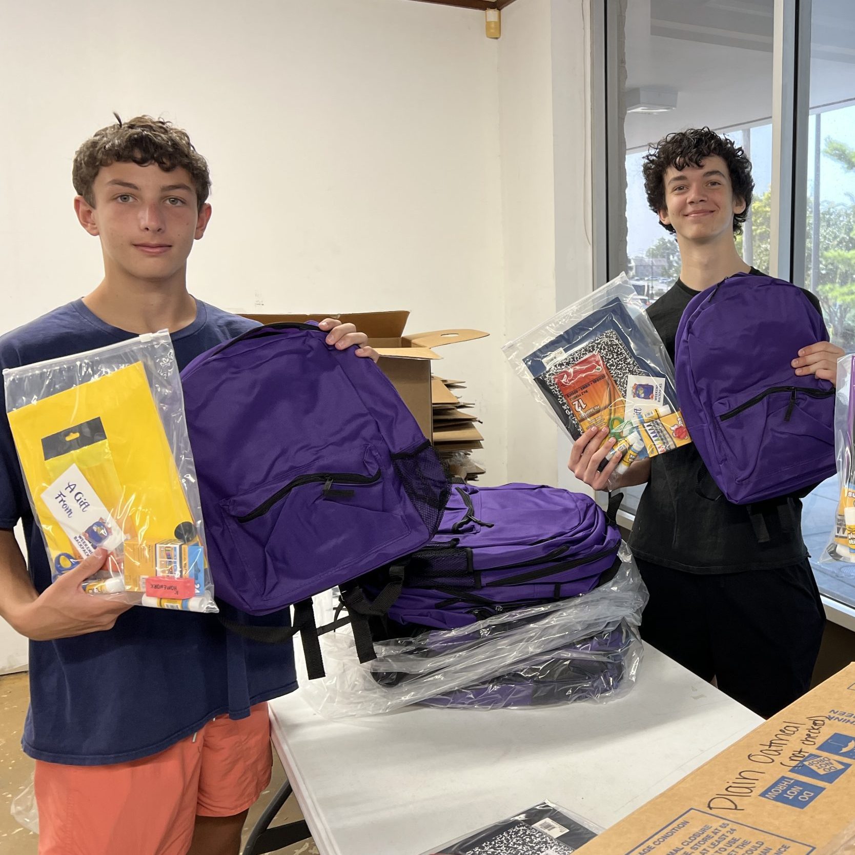 Two high school students packing backpacks with school supplies.