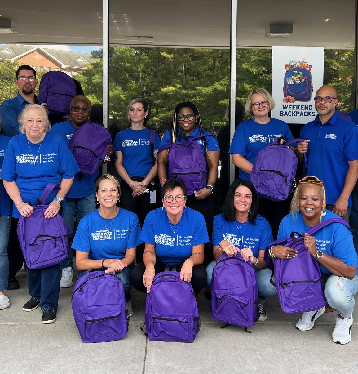 A group of people posed outside of Weekend Backpack's facility holding backpacks.