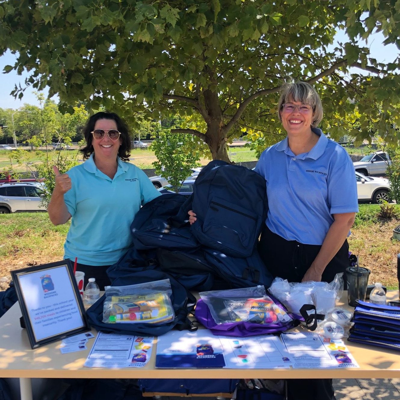 Two women outside standing behind a table with flyers, school supplies, and backpacks.