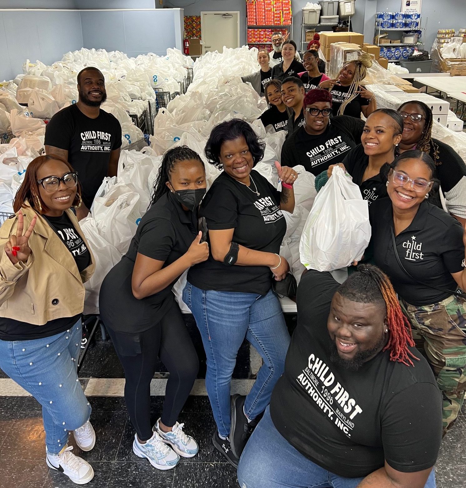 A group of people posed in front of a long table and rows of shopping carts filled with bags of food.