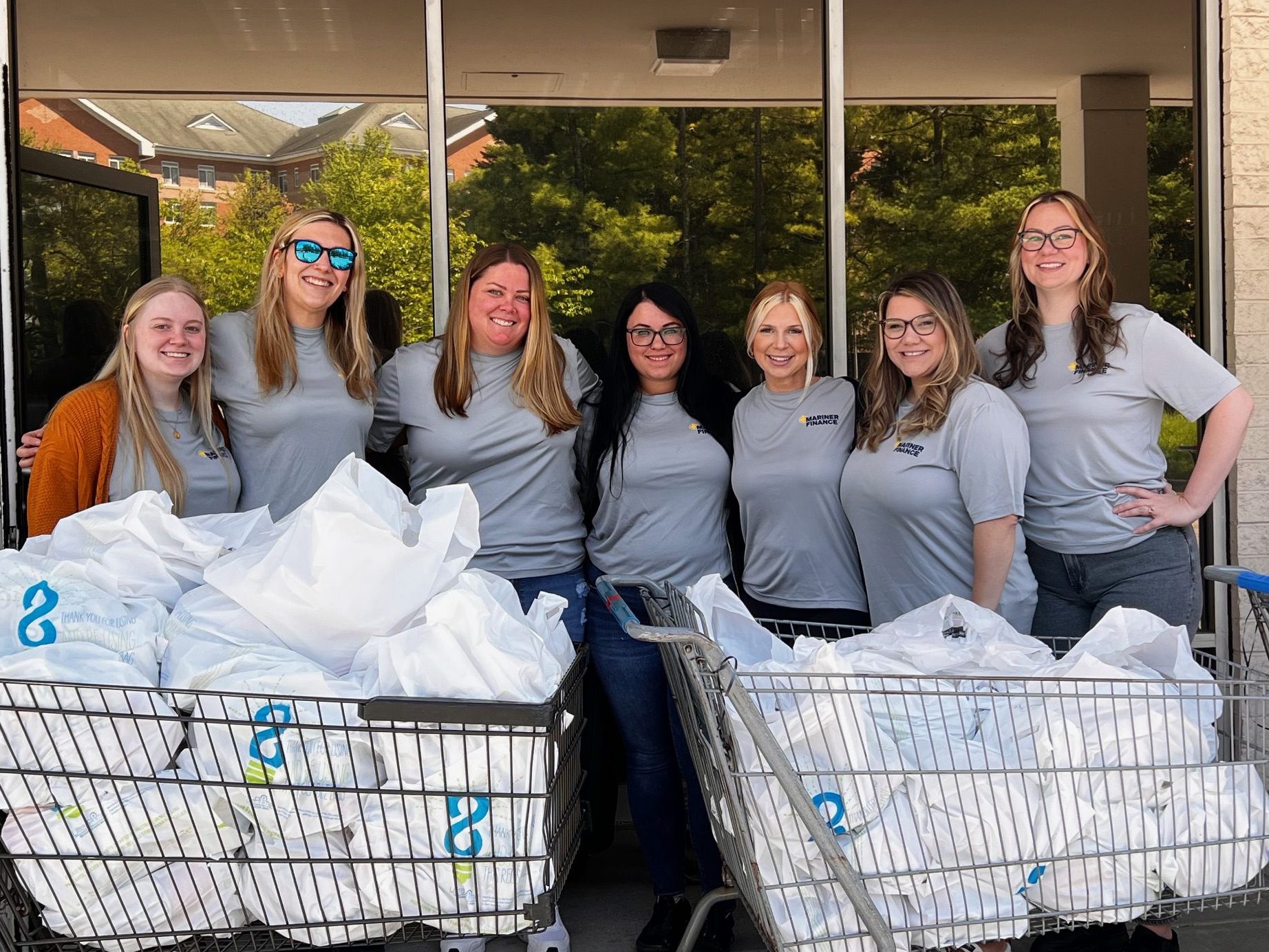 A group of women posed outside with shopping carts full of bags of food.